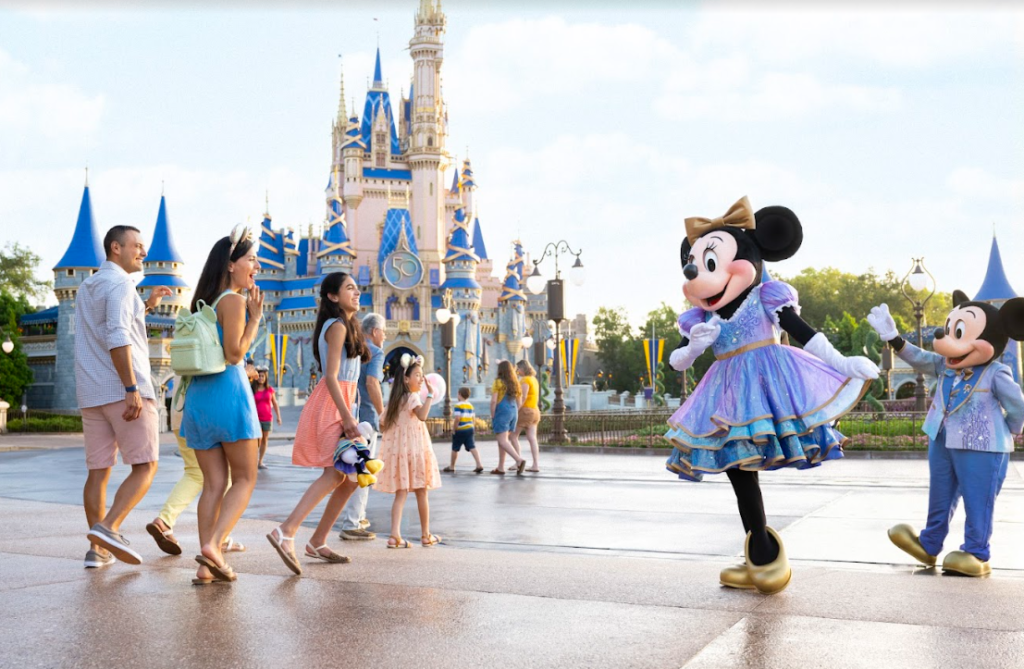 You can see two people dressed up as Mickey Mouse and a family passes by. A girl is all smiles and waves at the Mickey Mouse (people in the costumes.) At the backdrop are the castles, typical of Disneyland - which is a very sought after mid-term break destination for families with children 