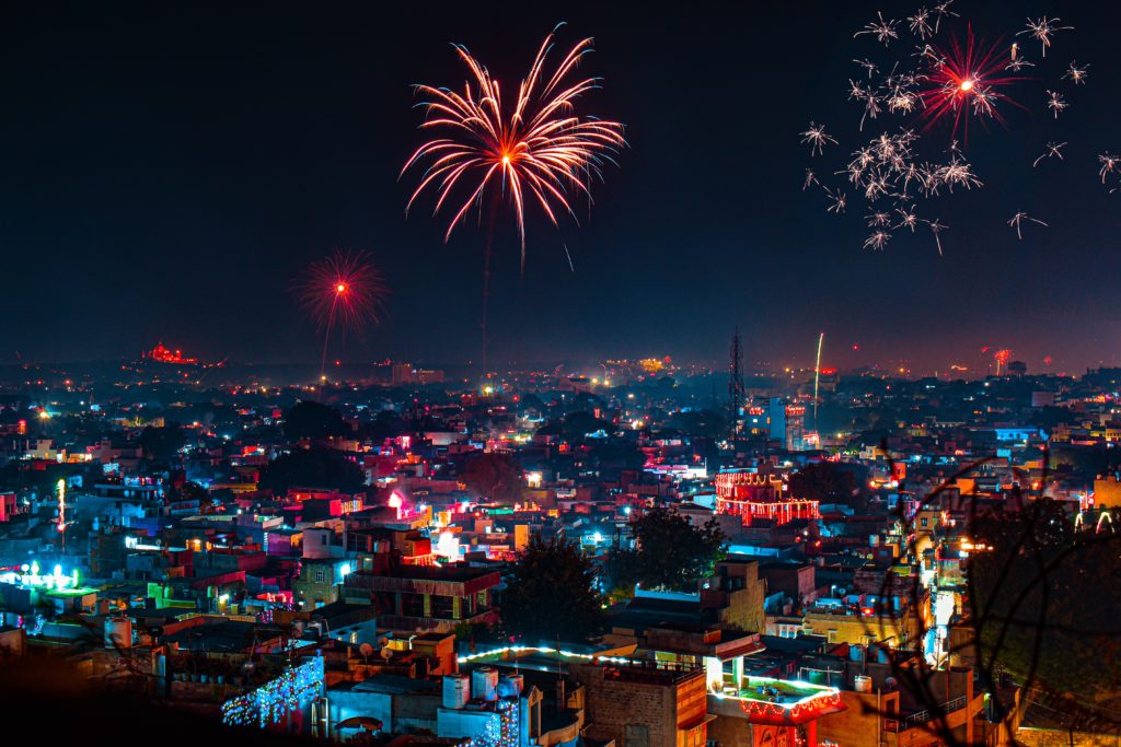 The photograph depicts a Diwali night sky that is awash with colourful fireworks. Diwali is a fall festival in India. You can also see the rooftops of houses (terraced houses) and they are all lit up with fairy lights, and clay lamps or diyas. 