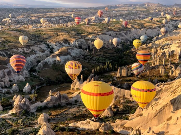 Various balloons are up in the air over the chimneys - the ones in the front are in yellow with a red band like pattern on them. In the background you can see the fairy chimneys and the valleys