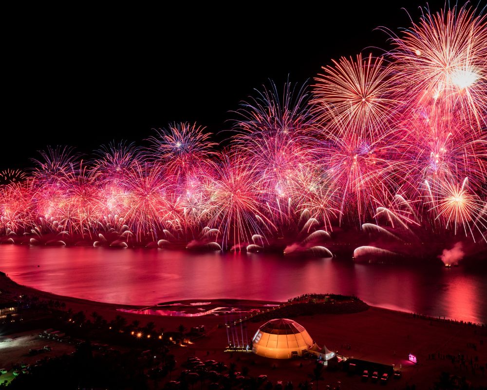 The entire photograph is in shades of pink - fireworks light up the Ras Al Khaimah landscape in the UAE. You can see a lit up dome too - that is in a shade of orange. The rest is all pink, the pink fireworks casting their light in the ocean below