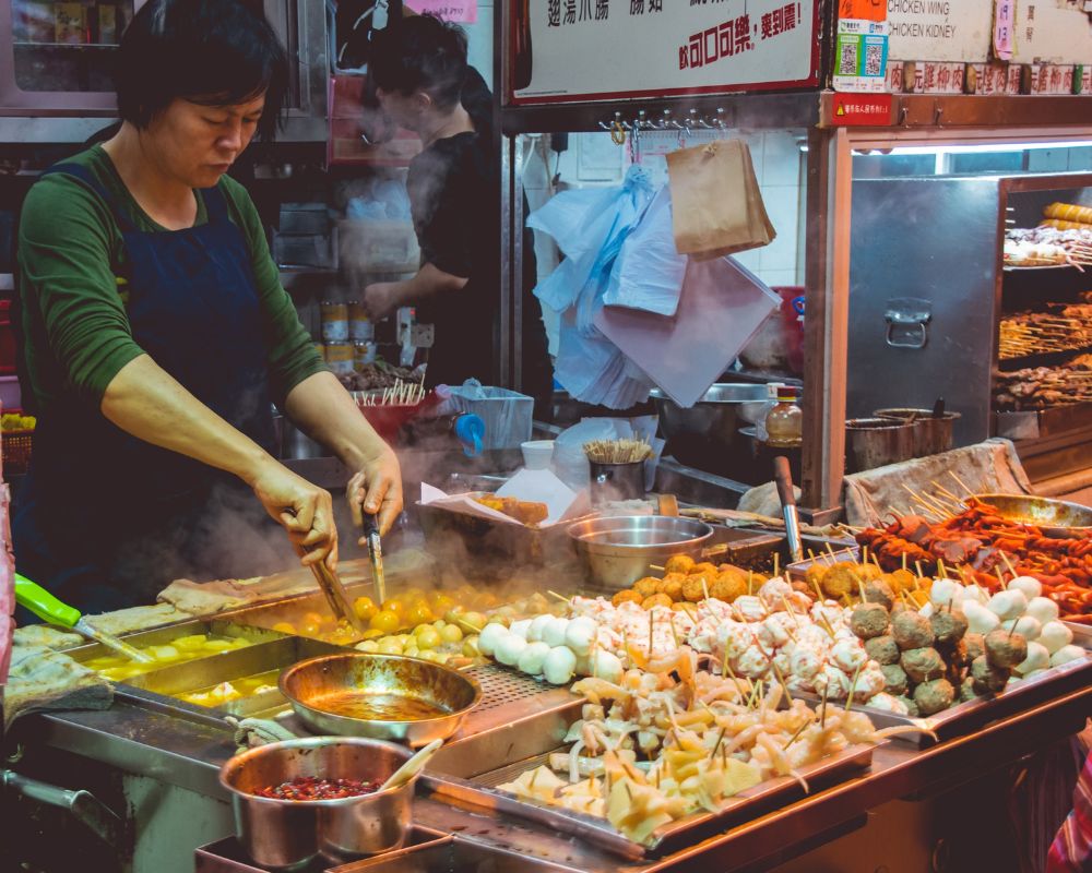 A woman has a counter in front of her. There are skewers with different kinds of meats, marinated in an assortment of spices and marinades. 