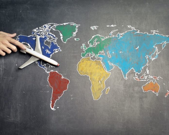 On a black chalk board various continents/ globe map is drawn with colours filled in. A toy plane sits on that board