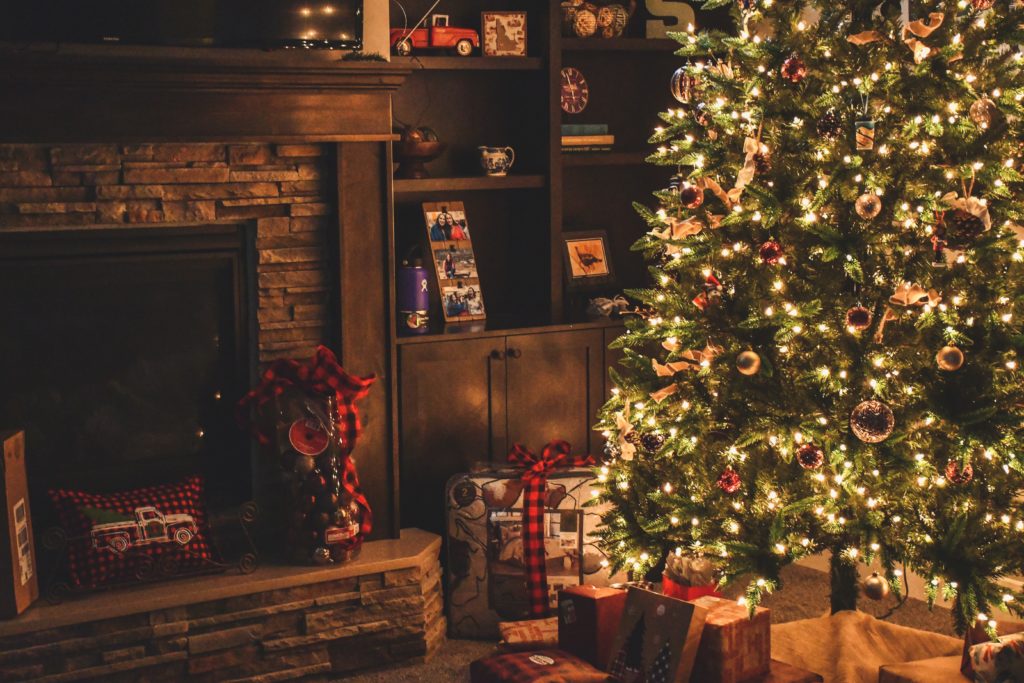 A room with Christmas tree all decorated, a fireplace that is not lit, gifts and fairy lights - various traditional colours and decor give a warm cosy look