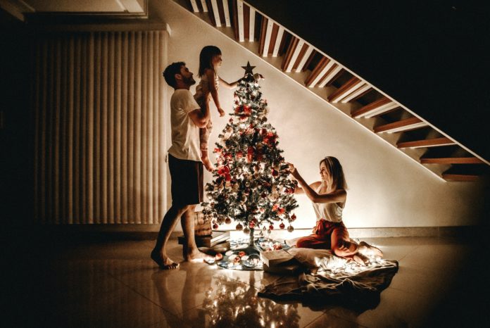 A family, according to their Christmas tradition decorates their tree at night, lifting their little girl to put a star on top