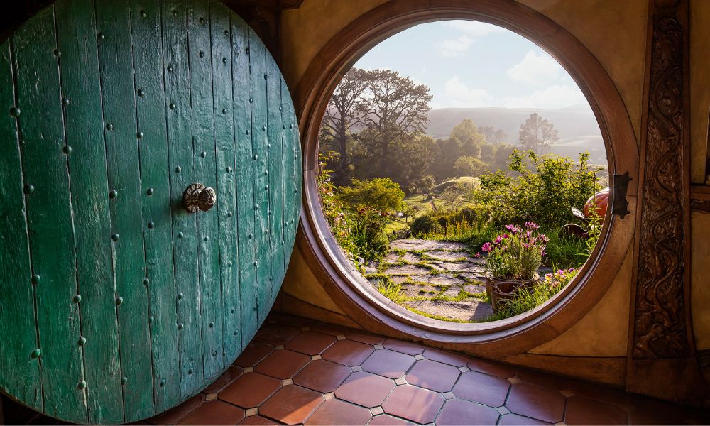 A circular green door opens to gorgeous views and a stone and grass pathway in Hobbiton 