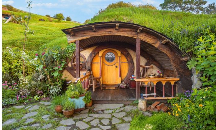 The outside of a Hobbit hole in Hobbiton - a yellow gate to the circular house with a garden and balcony of sorts