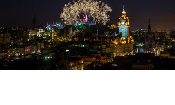 The city of Edinburgh during Hogmanay - you see fireworks in the sky, the cathedral and lights all around