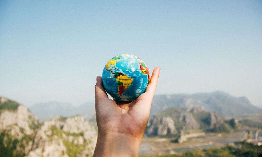 A man is holding a small globe in his hands and at the backdrop are mountains - a metaphorical or representative pic to symbolise future of air travel