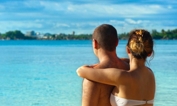 A man and a woman - their backs to the camera, sharing a romantic moment, looking out at the blue sea