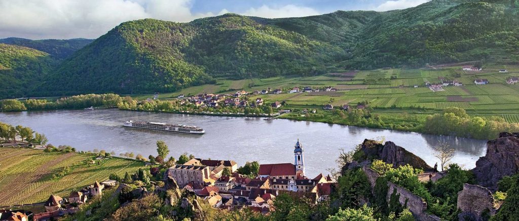 A river cruise gliding across a river that is flanked by green valleys and quaint cottages
