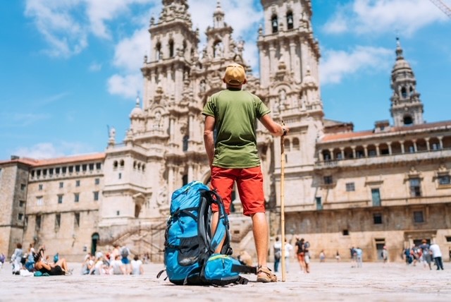 A man with his back to the camera, and a backpack at his feet and a walking stick in his hand on the Camino route