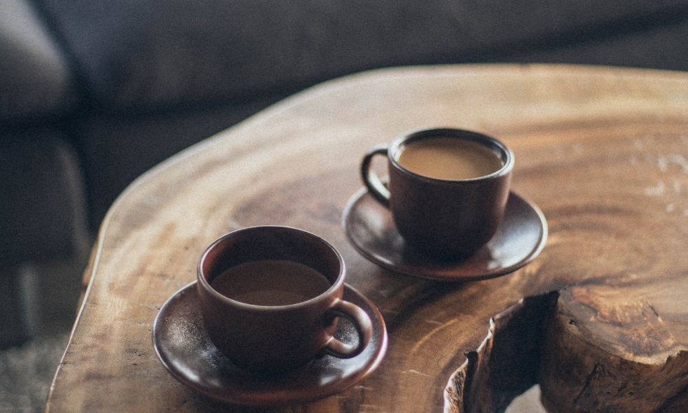 Two dark brown cups filled with Jamaican Blue Mountain Coffee and placed on a table made out of wodd