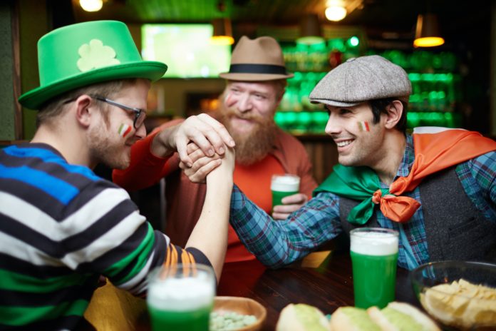 Men wearing green and with glasses full of green drinks celebrating St. Patrick's Day in a global setting