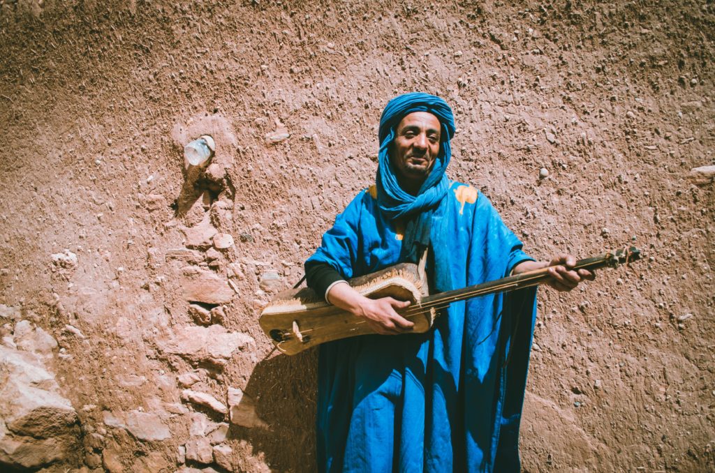 A Moroccan nan in a traditional blue costume playing an instrument 