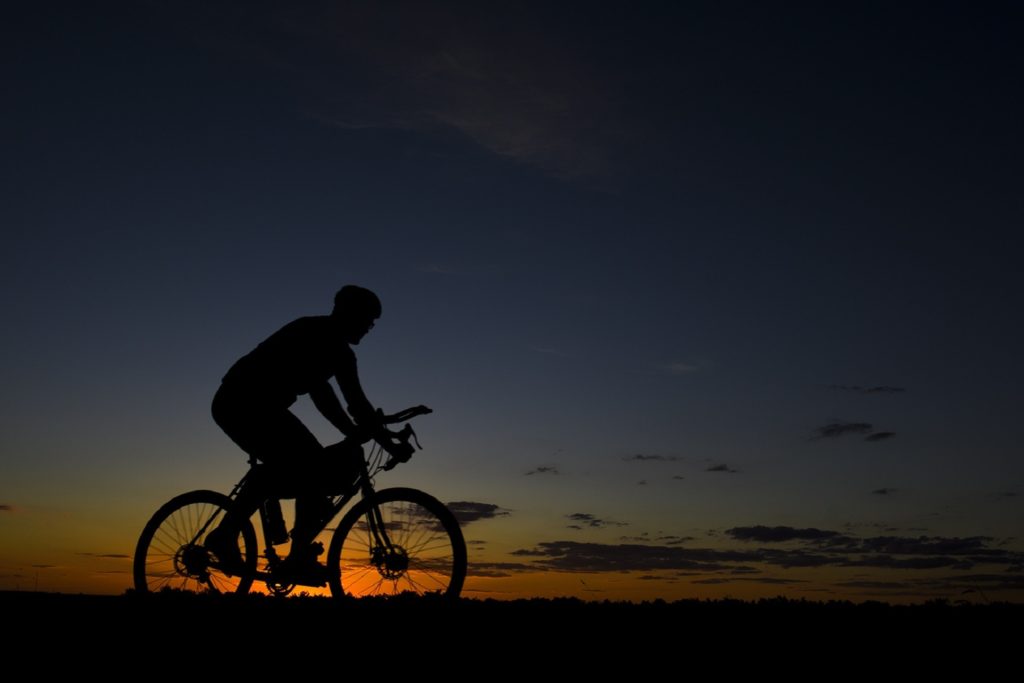 A man on a bicycle and behind him is a wonderful sunset